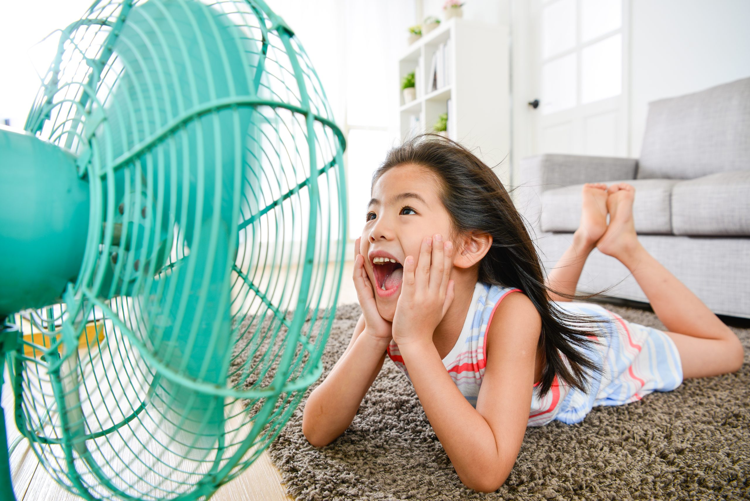 little girl lying down on floor in front of a fan